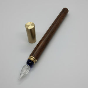 Ink pen with wooden handle, brass clip, and glass reservoir on a gray background